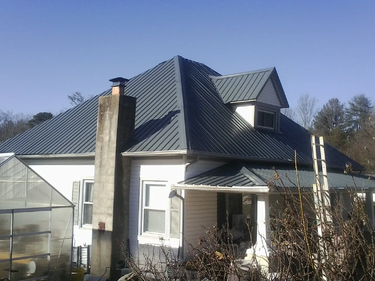 Dark blue standing seam metal roof on a white farmhouse with dormer — Slate & Tile Roof Repair by Roofing Brothers in Mill Spring