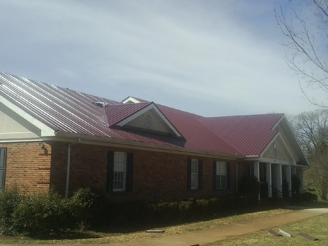 Red metal roof with gabled entries on a long brick building, from a Hail Damage Roof Repair job in Mill Spring
