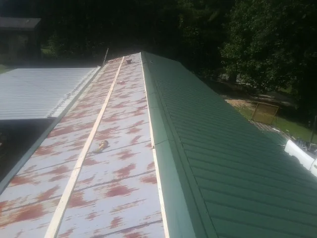 Old rusted panels beside newly installed green metal roofing — Wind Damage Roof Repair by Roofing Brothers in Mill Spring