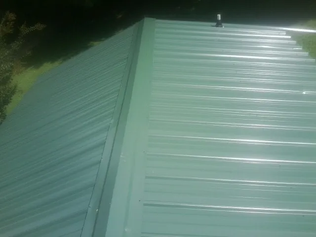 New green metal panels meeting at the ridge of a roof — Flat Roof Repair work by our crew in Mill Spring