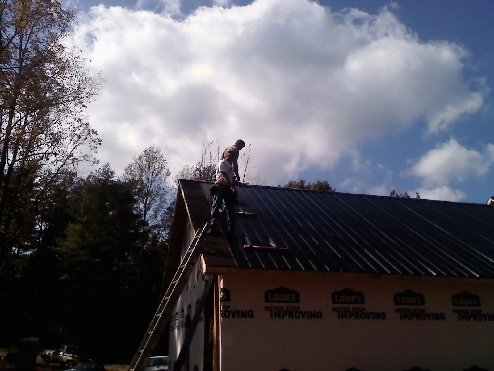 Roofer fastening dark metal panels high against a cloudy sky, from a Roof Inspection job in Mill Spring