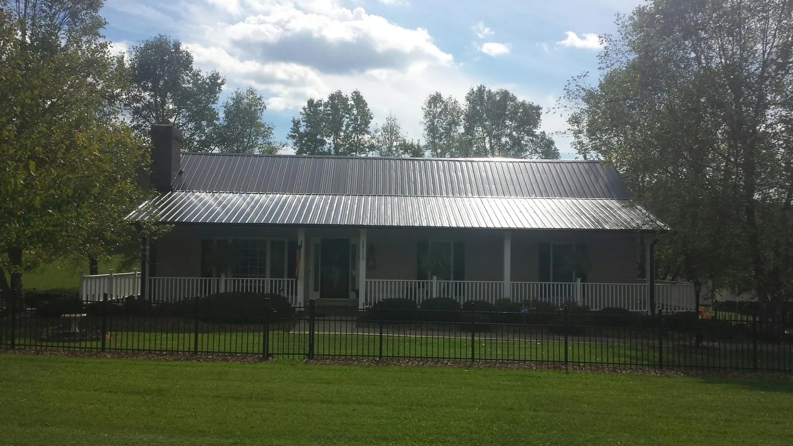 Gray metal roof on a brick ranch with a full width front porch — Gutter Guard Installation work by our crew in Mill Spring